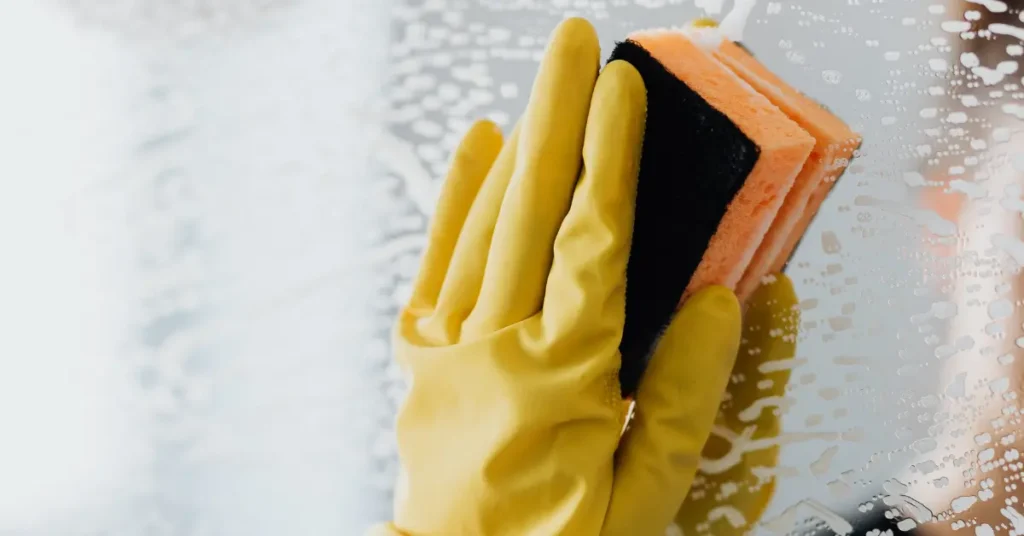 Commercial window cleaners scrubbing a glass surface with a sponge and wearing yellow rubber gloves.