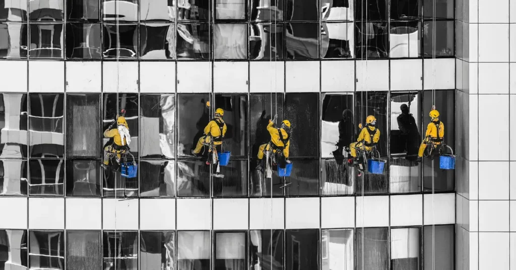 High-rise window cleaning company crew working on skyscraper windows using ropes, harnesses, and blue cleaning buckets.