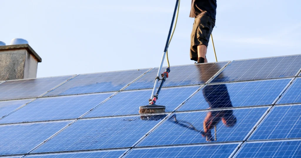 Professional solar panel cleaning using a rotating brush and water hose on rooftop solar panels.
