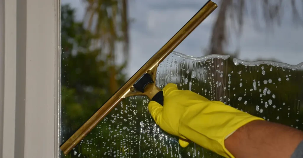 Residential window cleaners using a squeegee and wearing gloves to remove soap from a glass window.