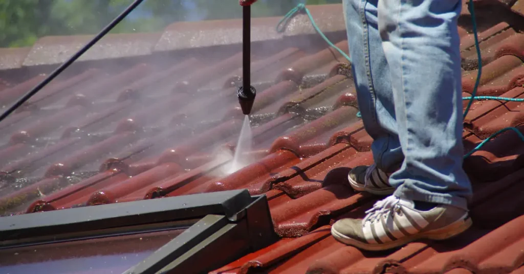 Exterior window cleaning using a pressure washer on a red tile roof surface.