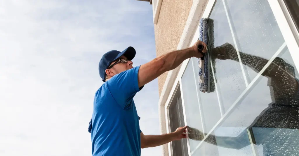 Outdoor window cleaner using a mop tool on a second-story residential window.